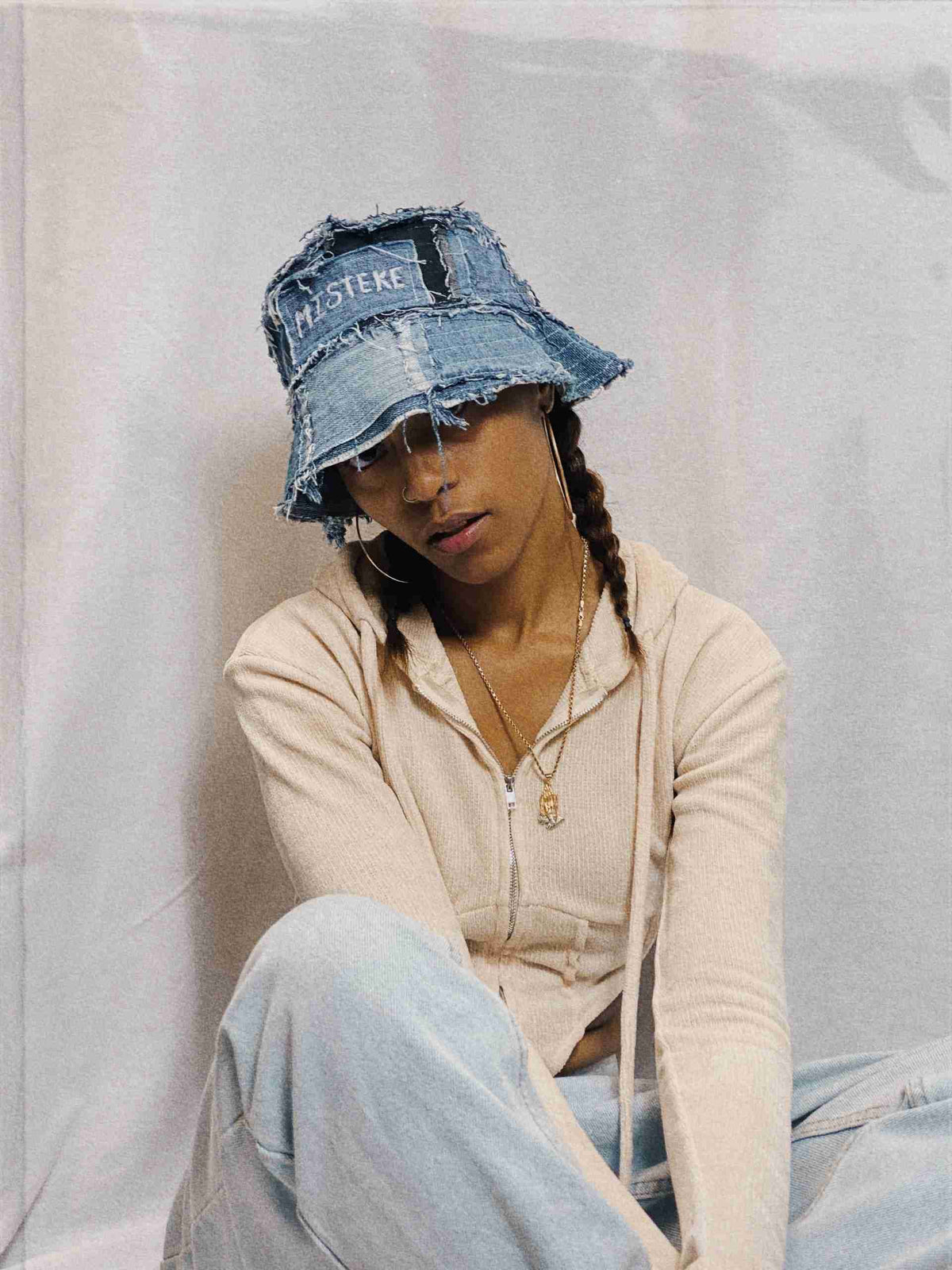 a woman sitting on the ground wearing a denim hat.