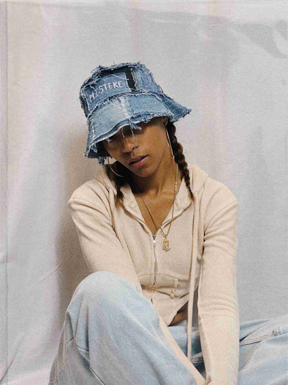 a woman sitting on the ground wearing a denim hat.