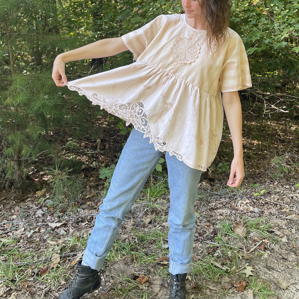 A woman standing in the woods wearing jeans and a blouse.