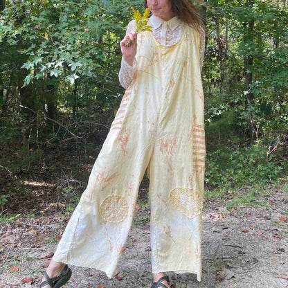 A woman is standing in the woods wearing a yellow jumpsuit.