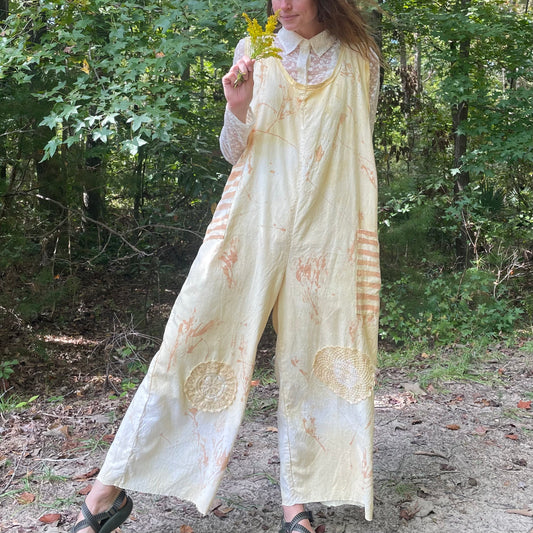 A woman is standing in the woods wearing a yellow jumpsuit.