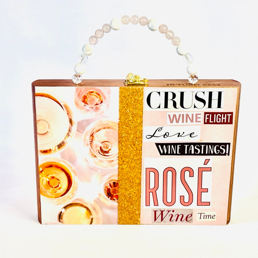 A stylish handbag designed to look like a wine-themed poster featuring rose and gold accents and a pearl handle.