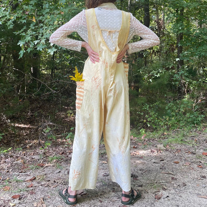 A woman in yellow overalls standing in the woods.