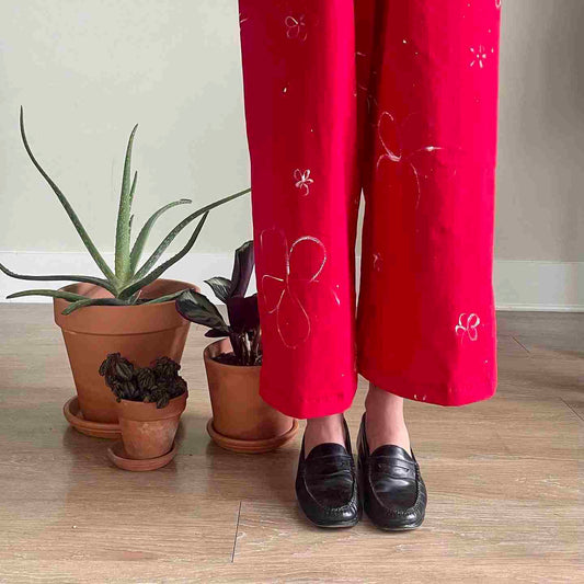 a woman in red pants standing next to a potted plant.