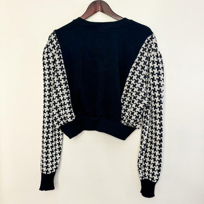 a black and white houndstooth sweater hanging on a hanger.