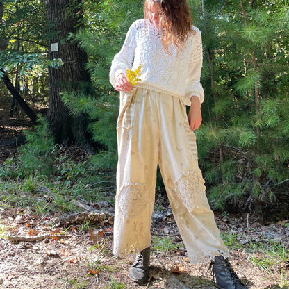 A woman is standing in the woods wearing a sweater and pants.