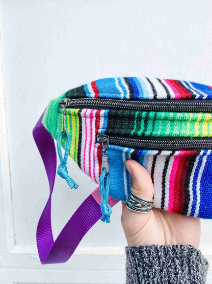 a hand holding a multicolored striped purse.
