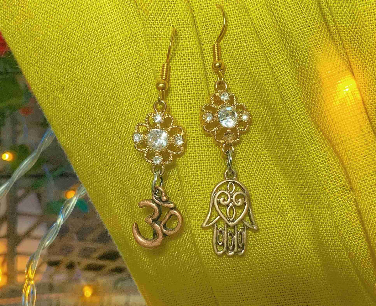a pair of gold earrings with a hamsa hanging from it.