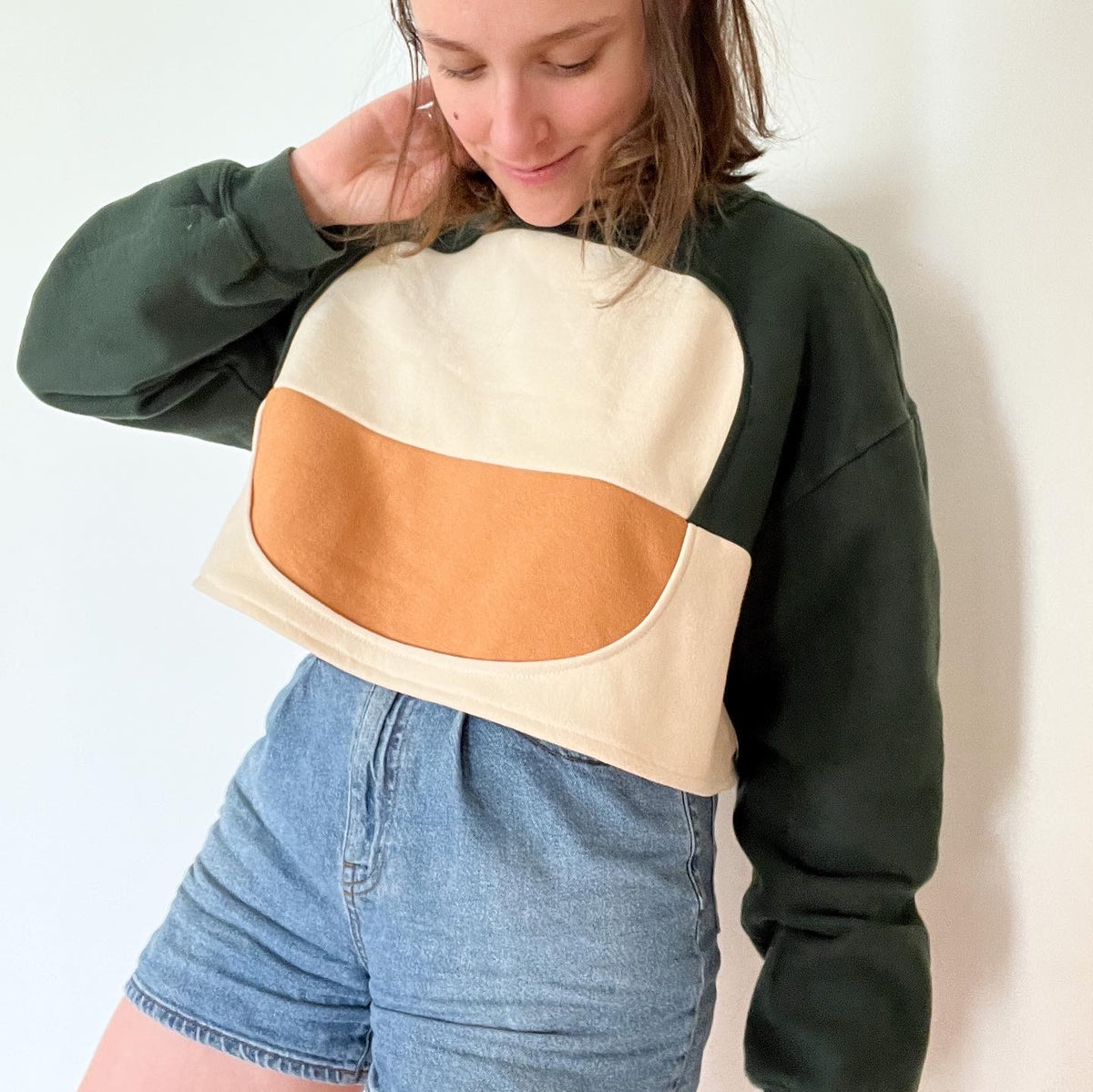A woman wearing the Sweatshirt of the Year Block Cropped Sweatshirt and denim shorts.
