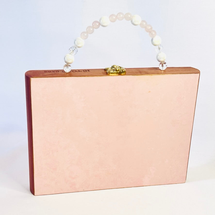A rectangular pink clutch purse with a pearl handle and gold clasp, displayed against a white background.