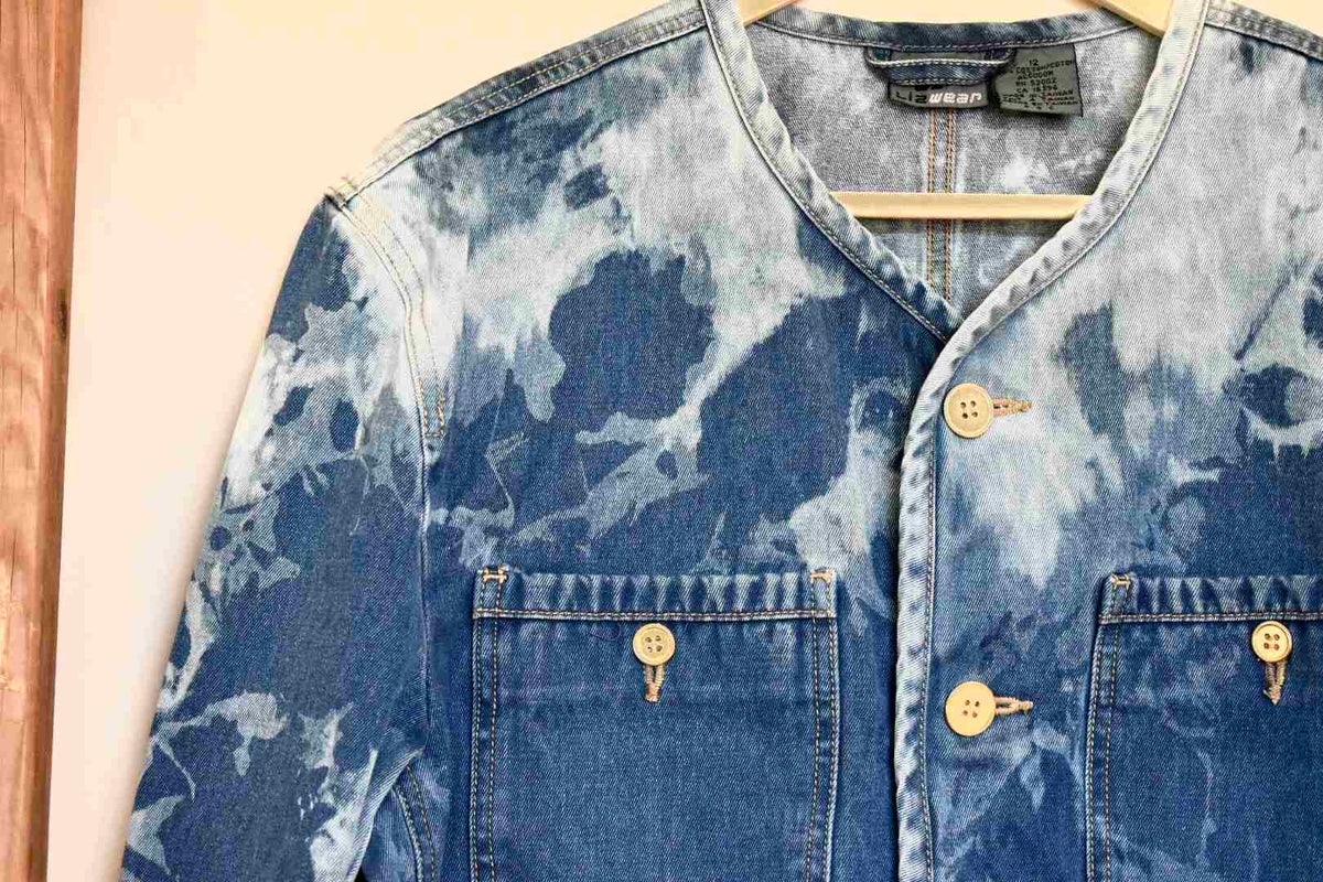 a blue jean jacket hanging on a wooden hanger.