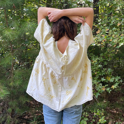 A woman standing in the woods wearing a yellow blouse.
