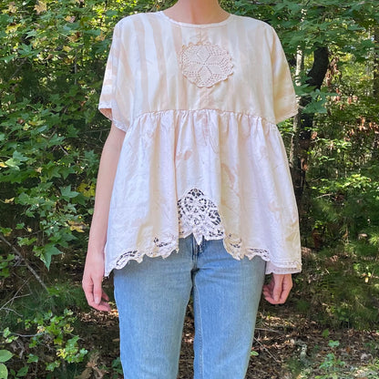 A woman is standing in the woods wearing a pink blouse.