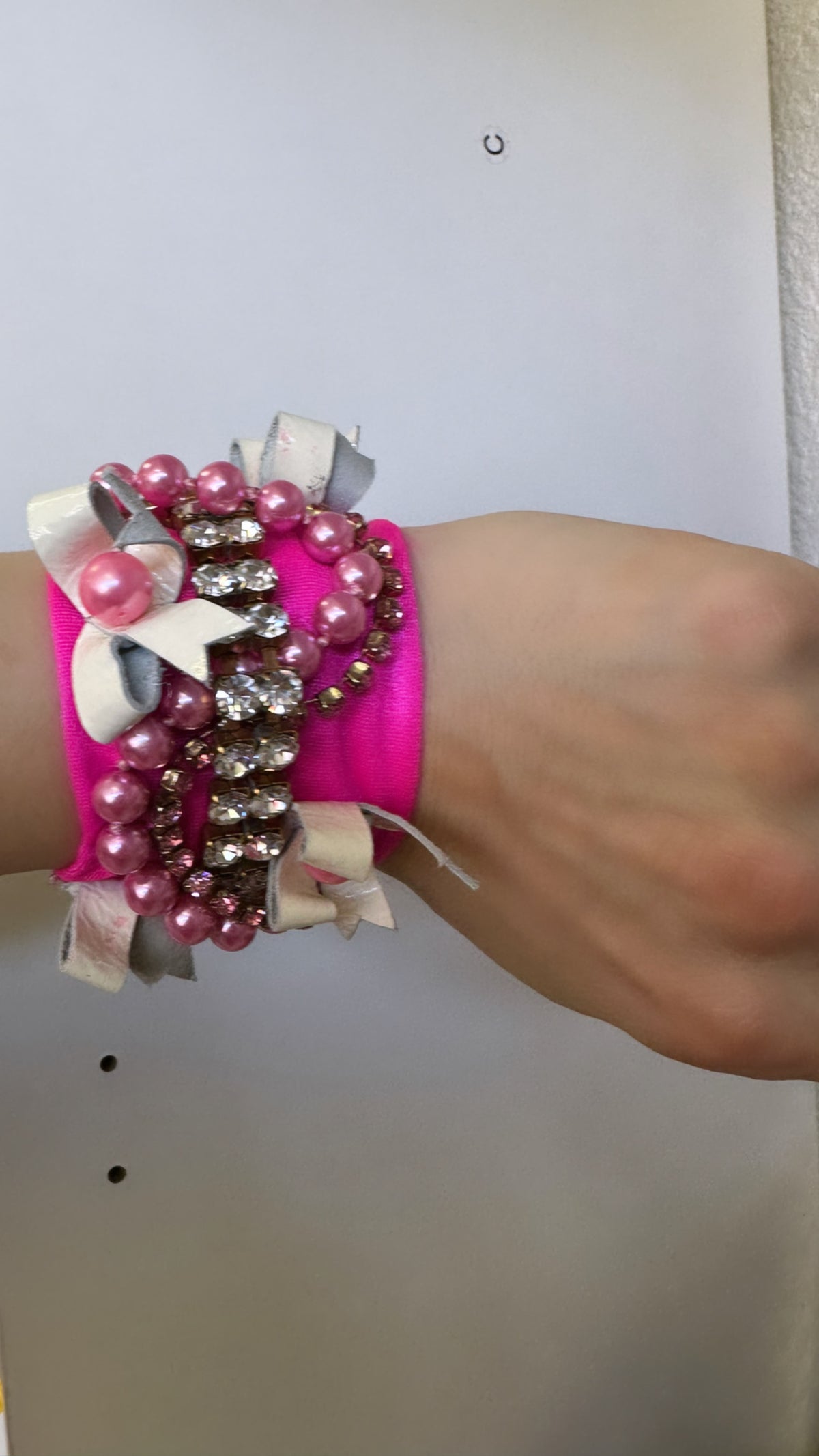 A person wearing a pink bracelet with pearls on it.