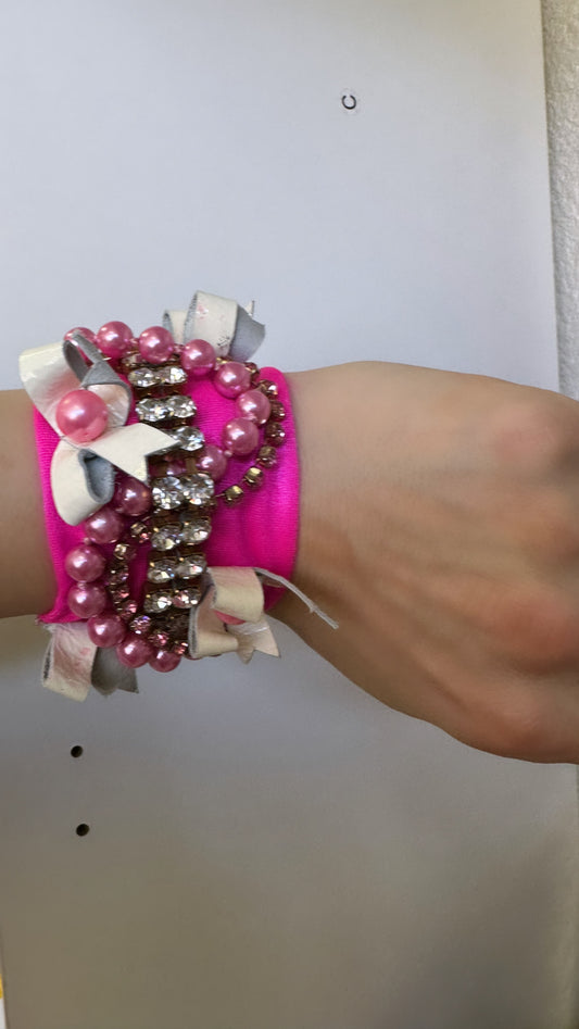 A person wearing a pink bracelet with pearls on it.