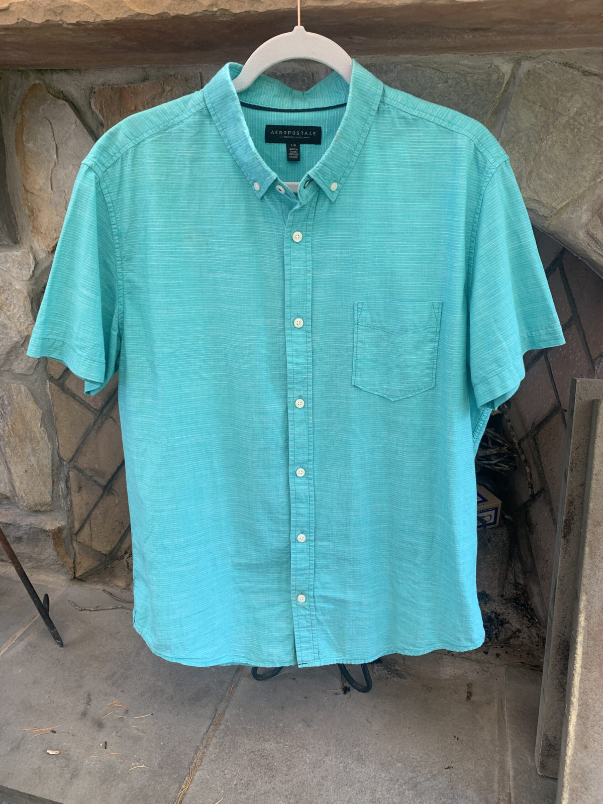 A Rolling Stones logo aqua button up shirt hanging on a clothes rack.