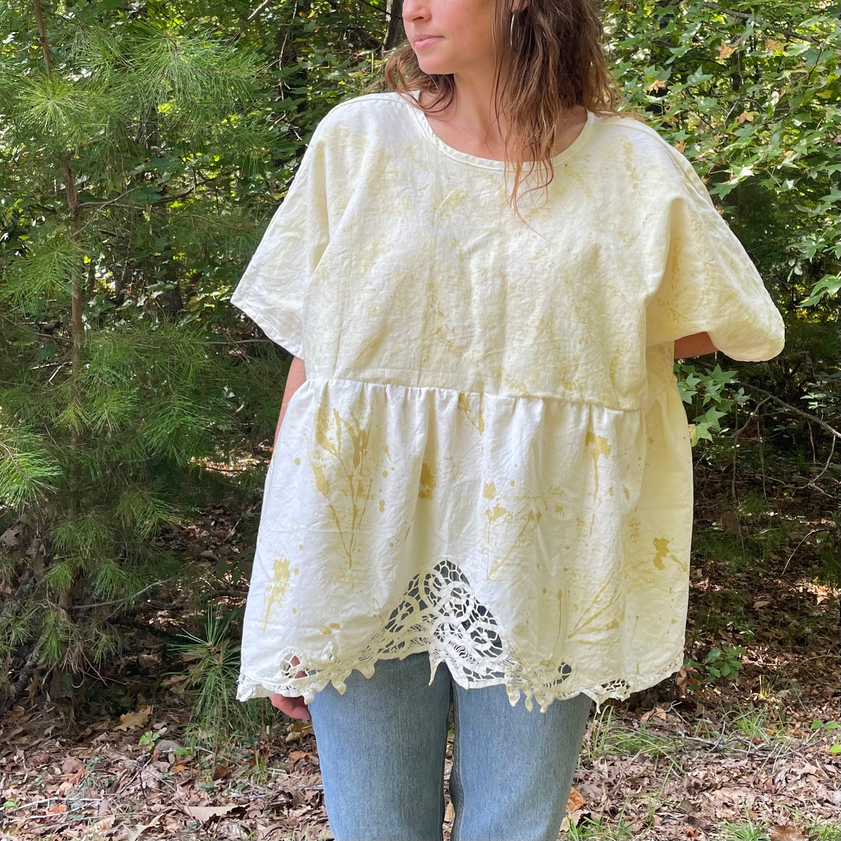 A woman is standing in the woods wearing a yellow blouse.