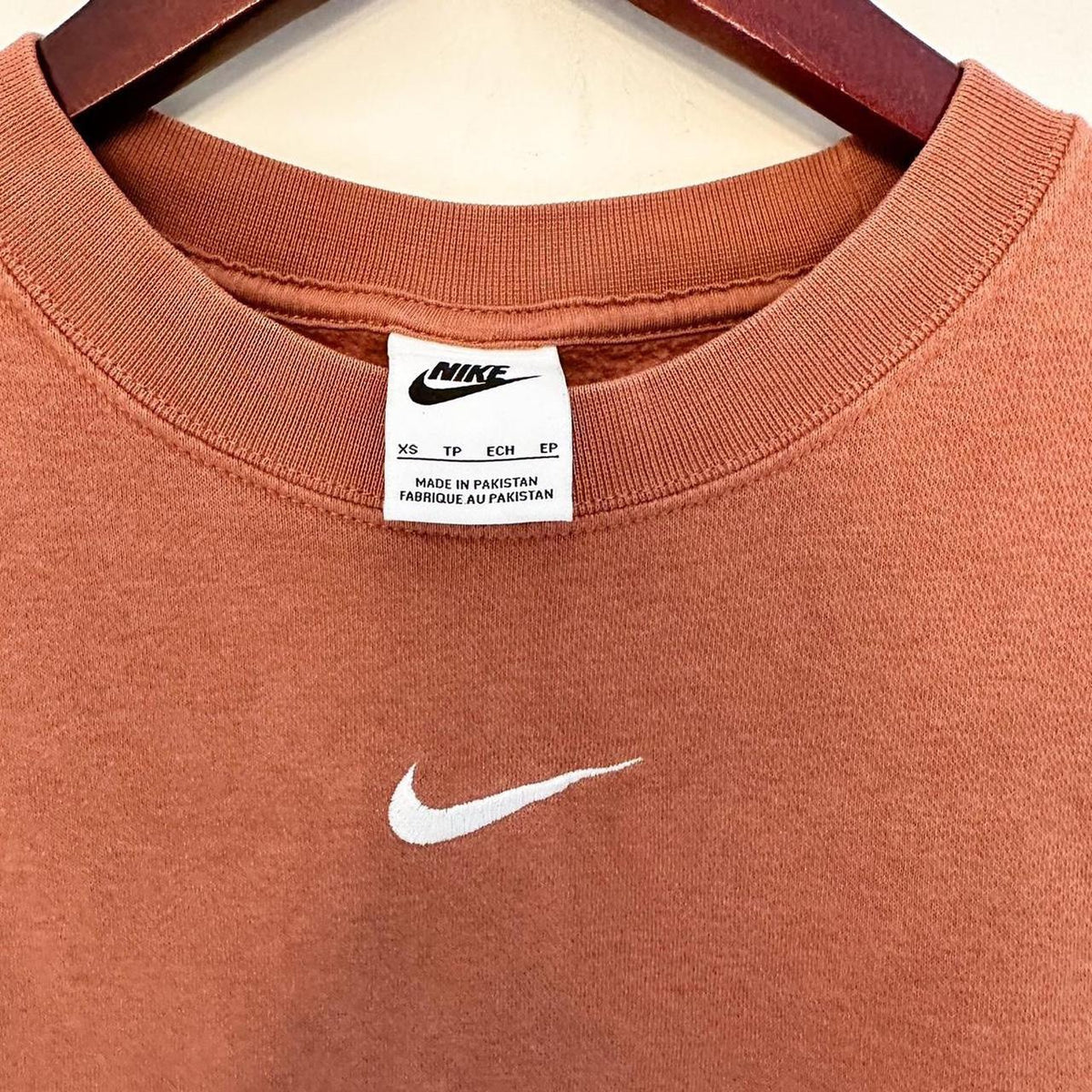 An orange nike t - shirt hanging on a hanger.