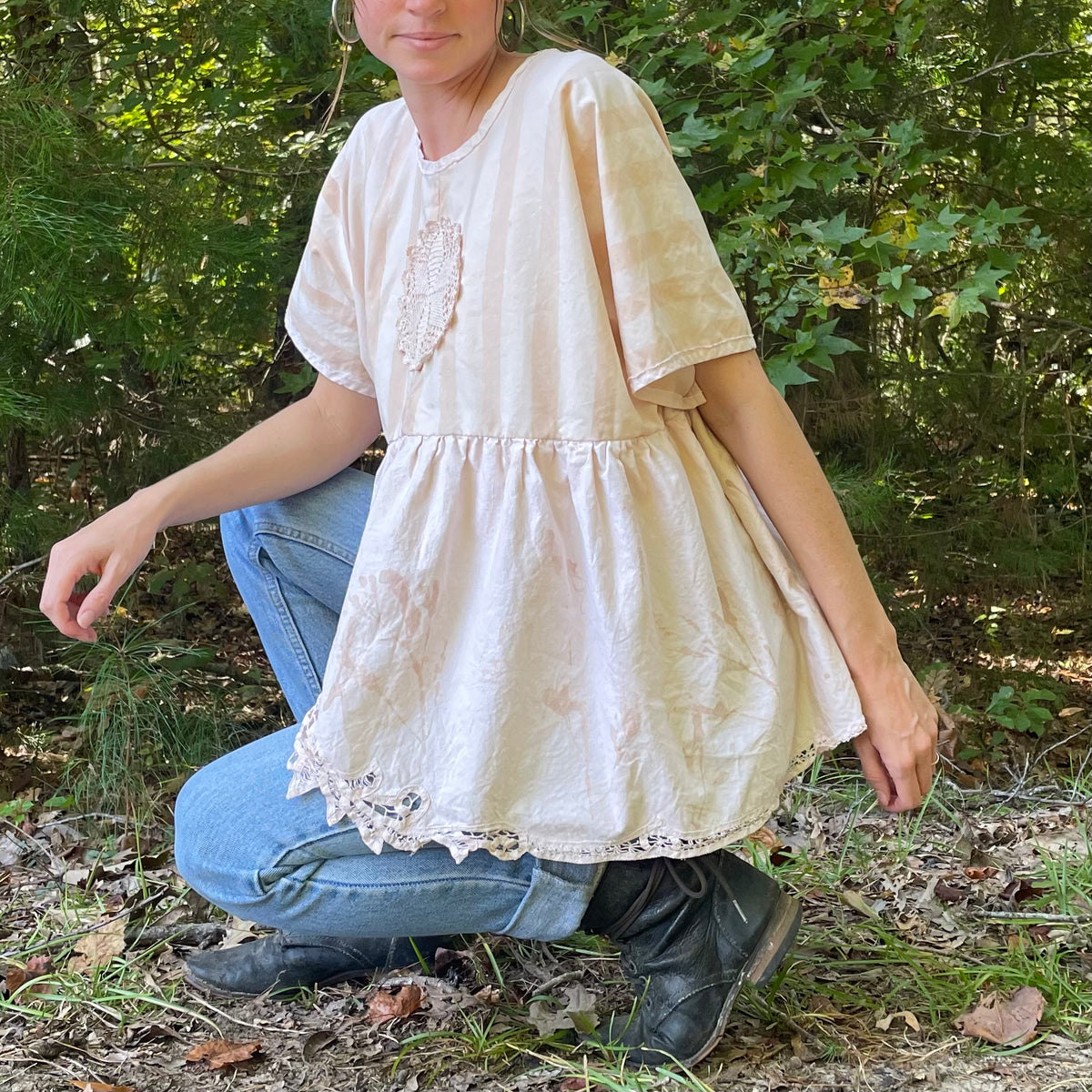 A woman crouching down in the woods wearing a blouse.