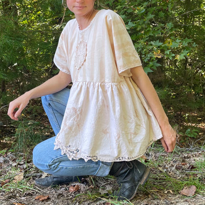 A woman crouching down in the woods wearing a blouse.