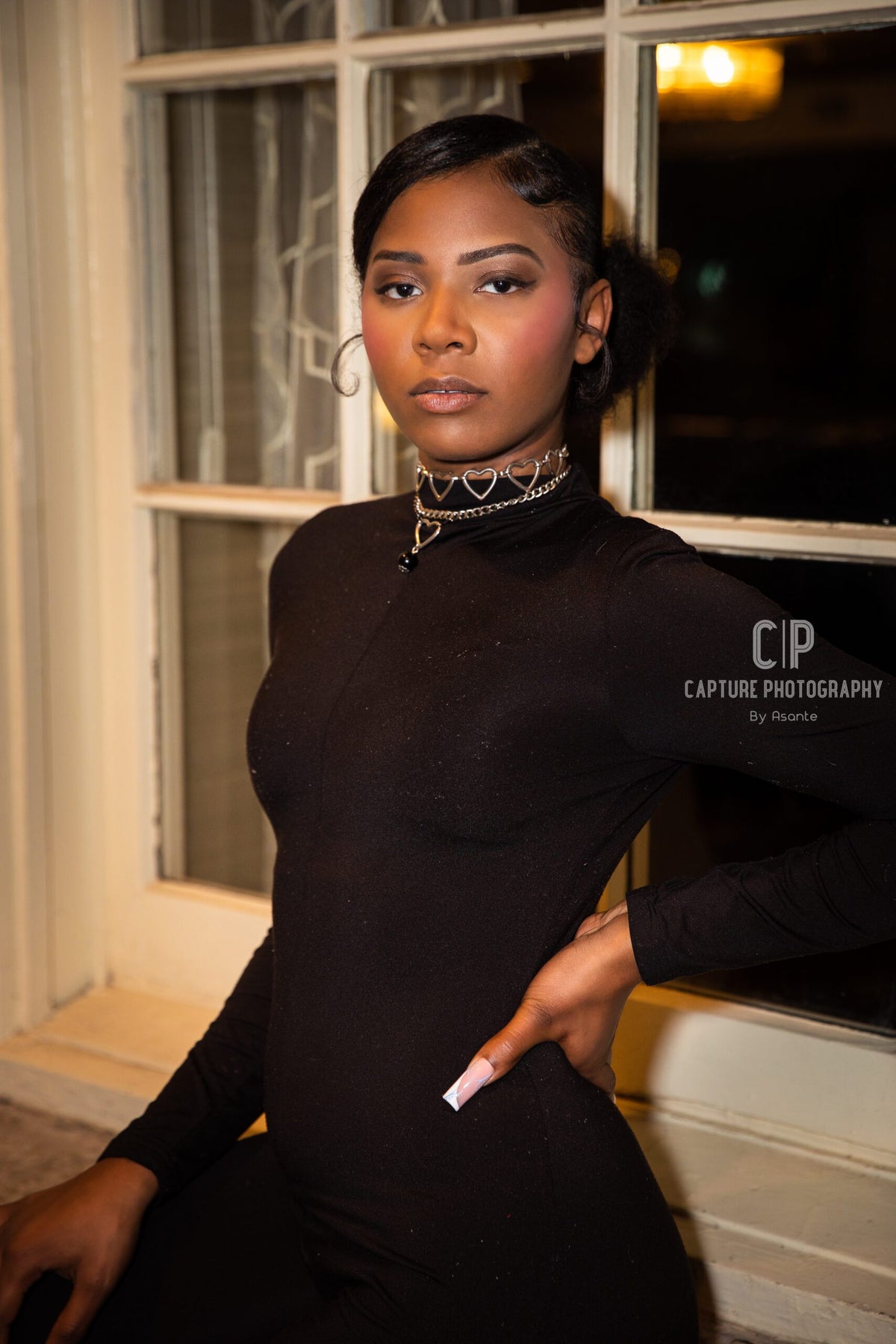 a woman is posing in front of a window.