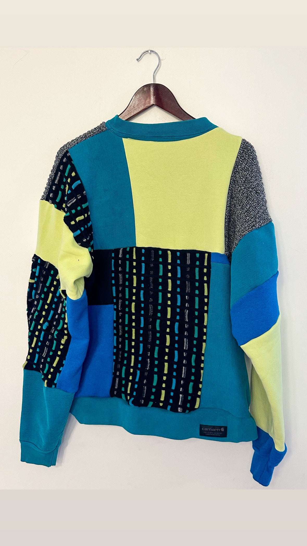 A blue, yellow, and black sweater hanging on a wall.