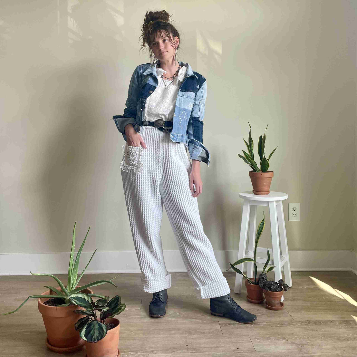 a woman standing in front of a wall next to potted plants.