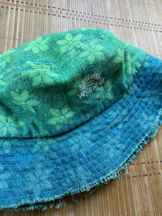 A green and blue bucket hat on a bamboo mat.