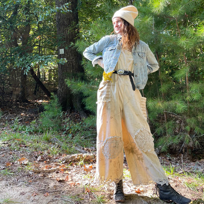 A woman is standing in the woods wearing a denim jacket and wide-legged pants.