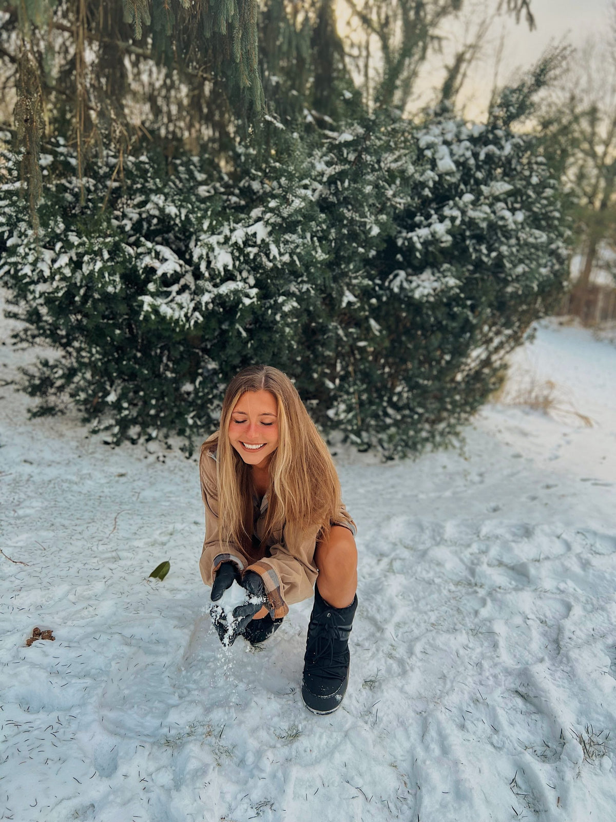 a woman kneeling in the snow wearing the Out in the Country 2pc set (Camel Flannel paired with 70s tawny earth tone stripes) with a snowboard.