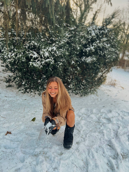 a woman kneeling in the snow wearing the Out in the Country 2pc set (Camel Flannel paired with 70s tawny earth tone stripes) with a snowboard.
