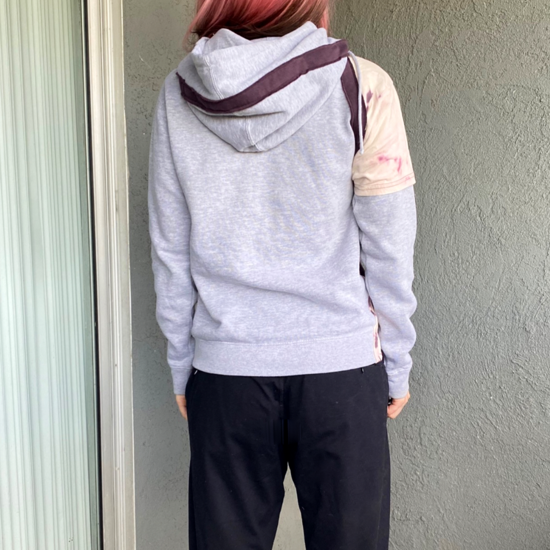 A woman with pink hair wearing a grey hoodie.