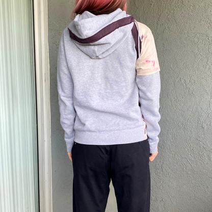 A woman with pink hair wearing a grey hoodie.
