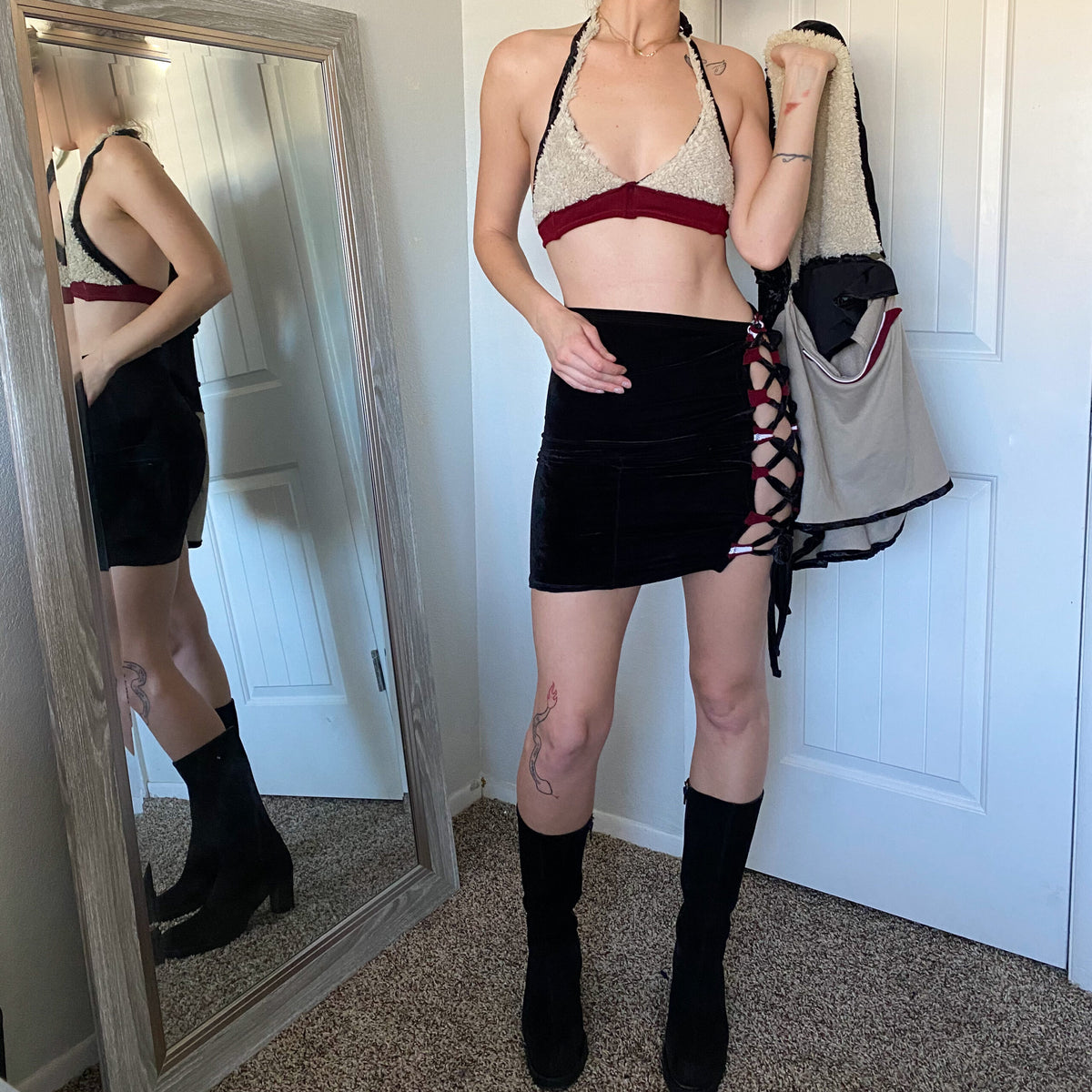 A woman is standing in front of a mirror wearing a bra and skirt.
