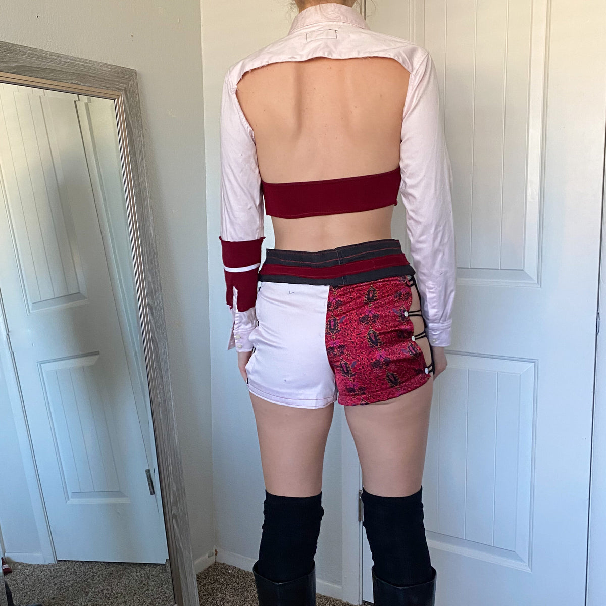 A woman is standing in front of a mirror wearing shorts and thigh high boots.