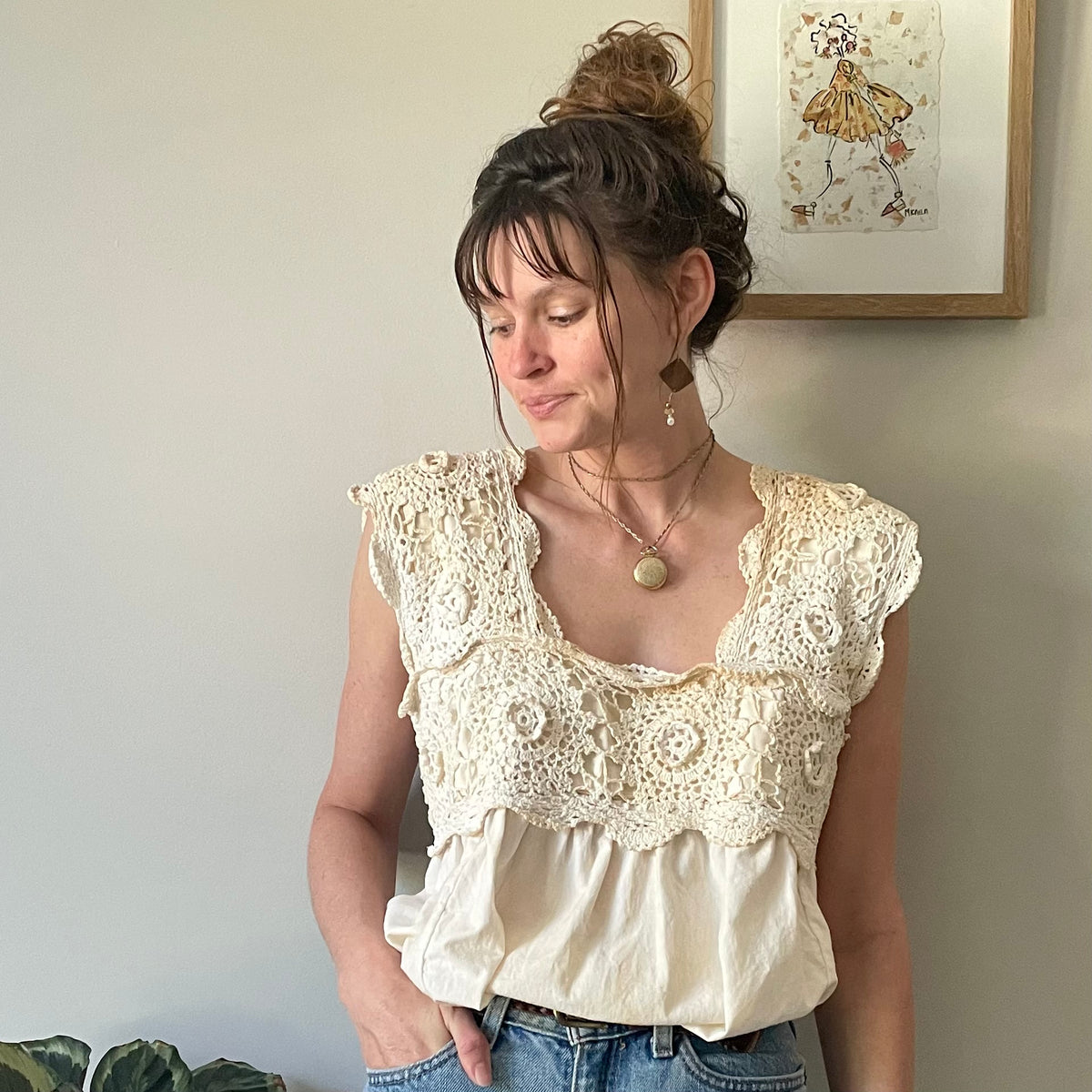A woman standing in front of a white wall wearing the Tea Stained Cream Crochet Festival Tank Top w/ Tie Back.
