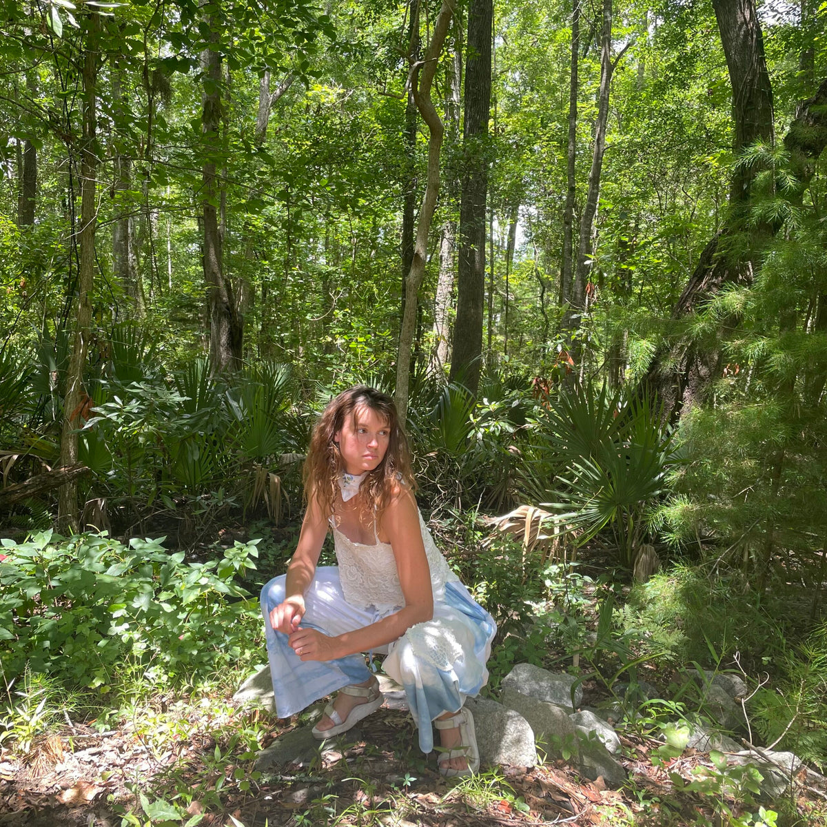 A woman crouching on a rock in the woods.