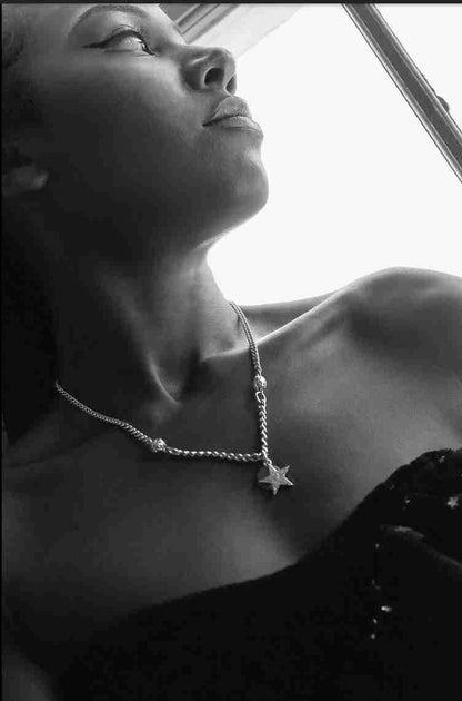 a woman in a black dress is wearing a star necklace.