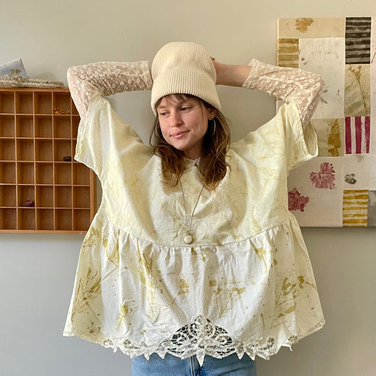 A woman posing with her hands on her head. Wearing a naturally dyed top.