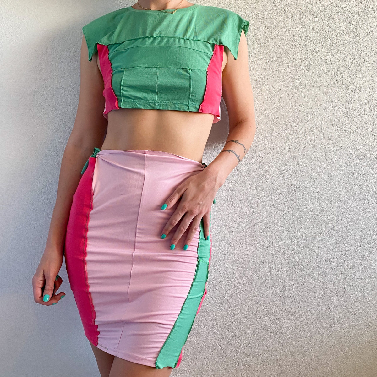 A woman wearing a 1of1 mint pink berry crop top and skirt set.