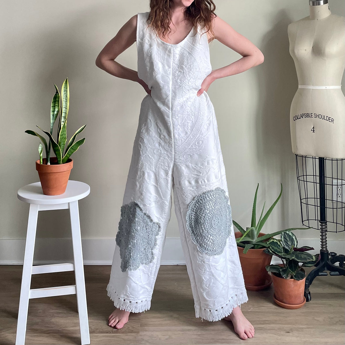 A woman in a white jumpsuit standing next to a plant.