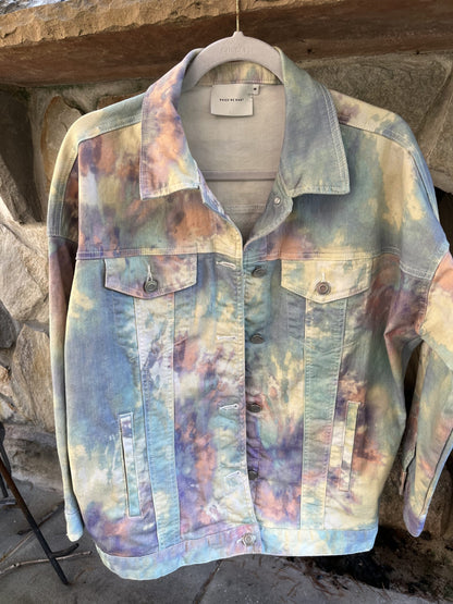 A tie dyed denim jacket hanging on a hanger.