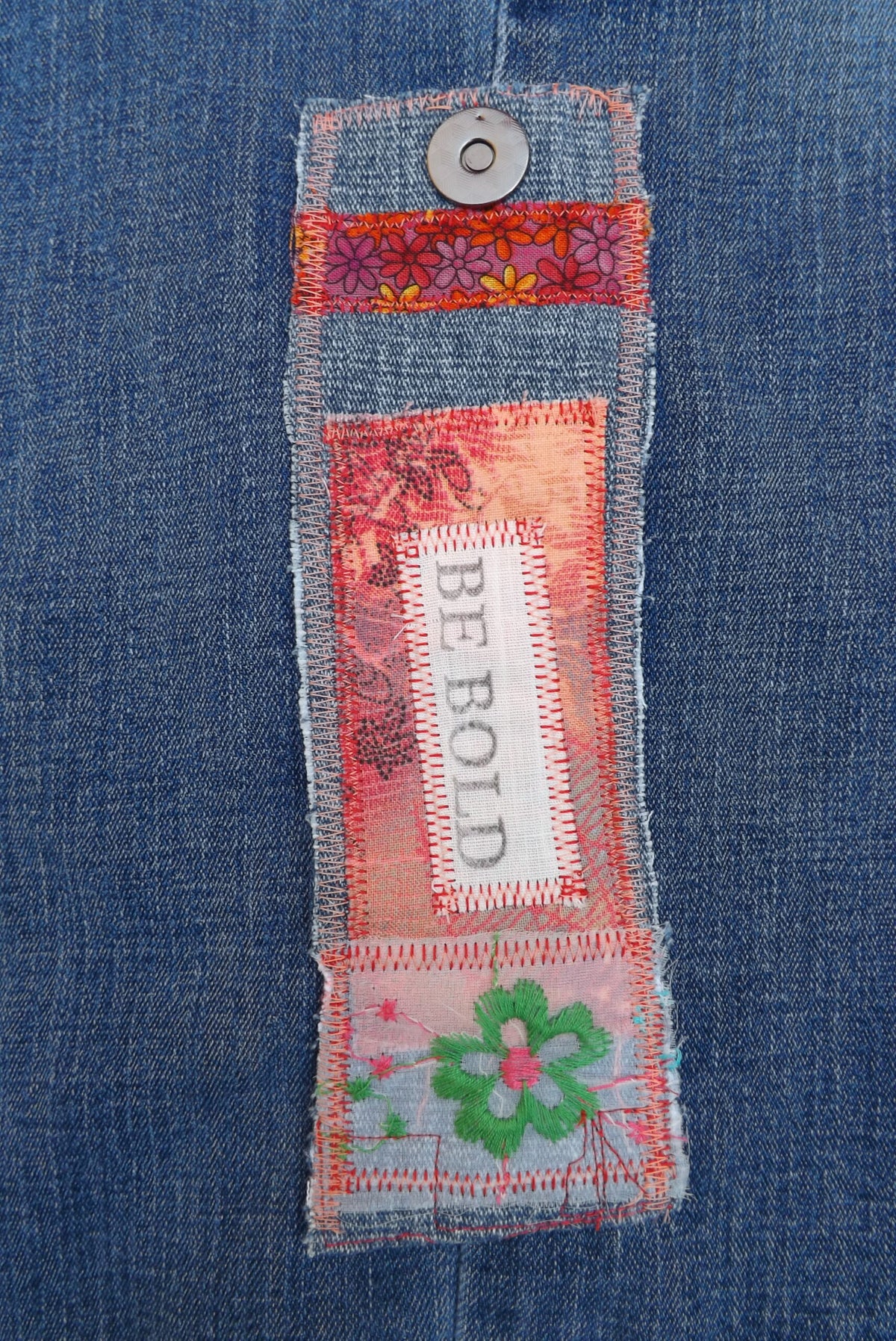 A denim cuff bracelet with Be Bold stamped on it and lace flowers.