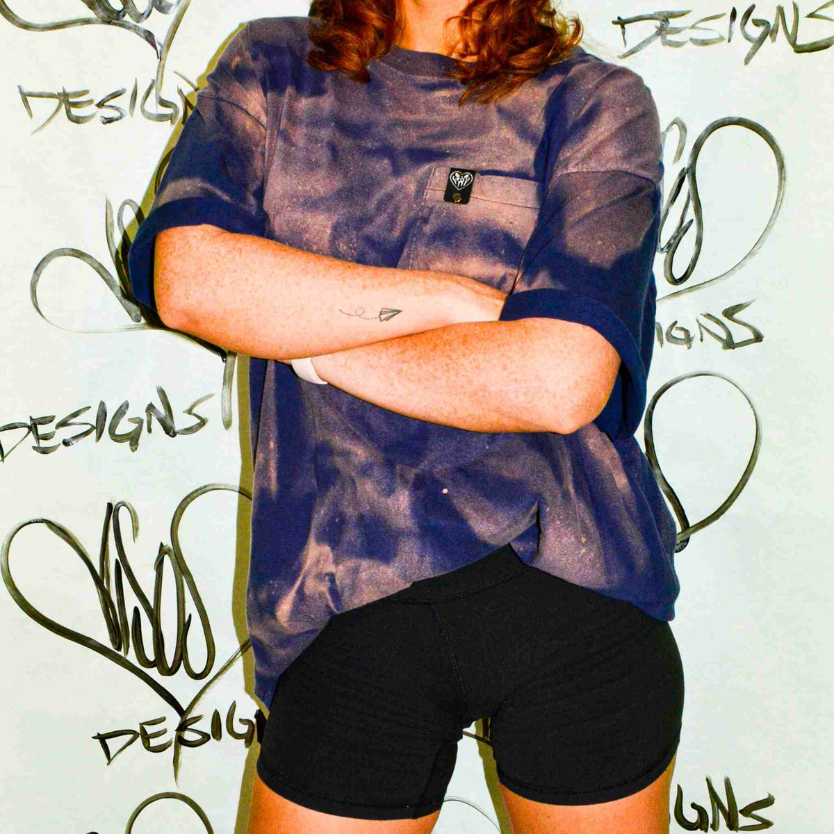 a woman with her arms crossed standing in front of a wall.