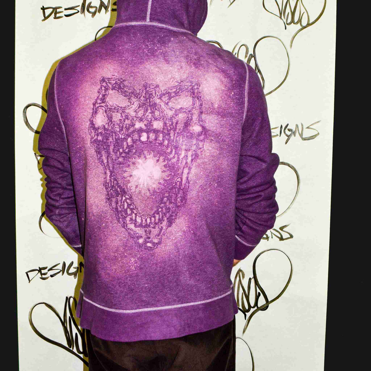 a man in a purple hoodie standing in front of a wall.