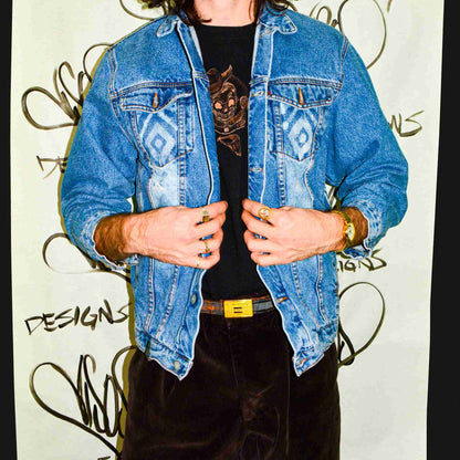 a man wearing a jean jacket standing in front of a wall.