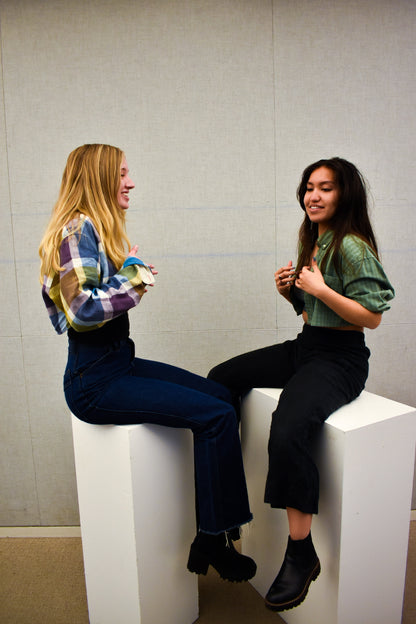 Two young women sitting on top of white pedestals while wearing Caterpillar Picnic (green and white checkered two-piece set).