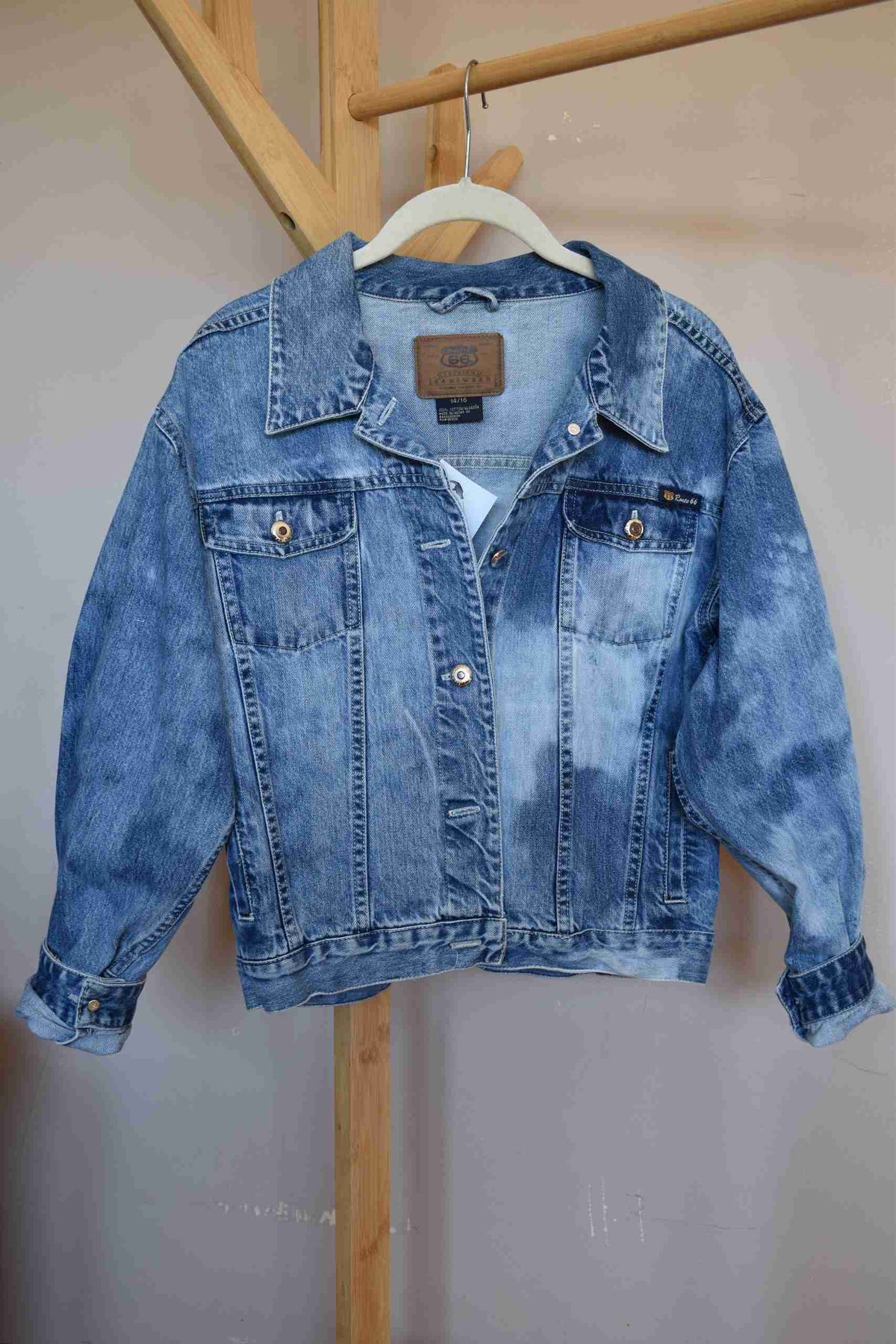 a blue jean jacket hanging on a wooden rail.
