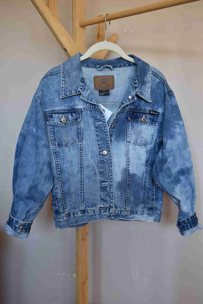 a blue jean jacket hanging on a wooden rail.