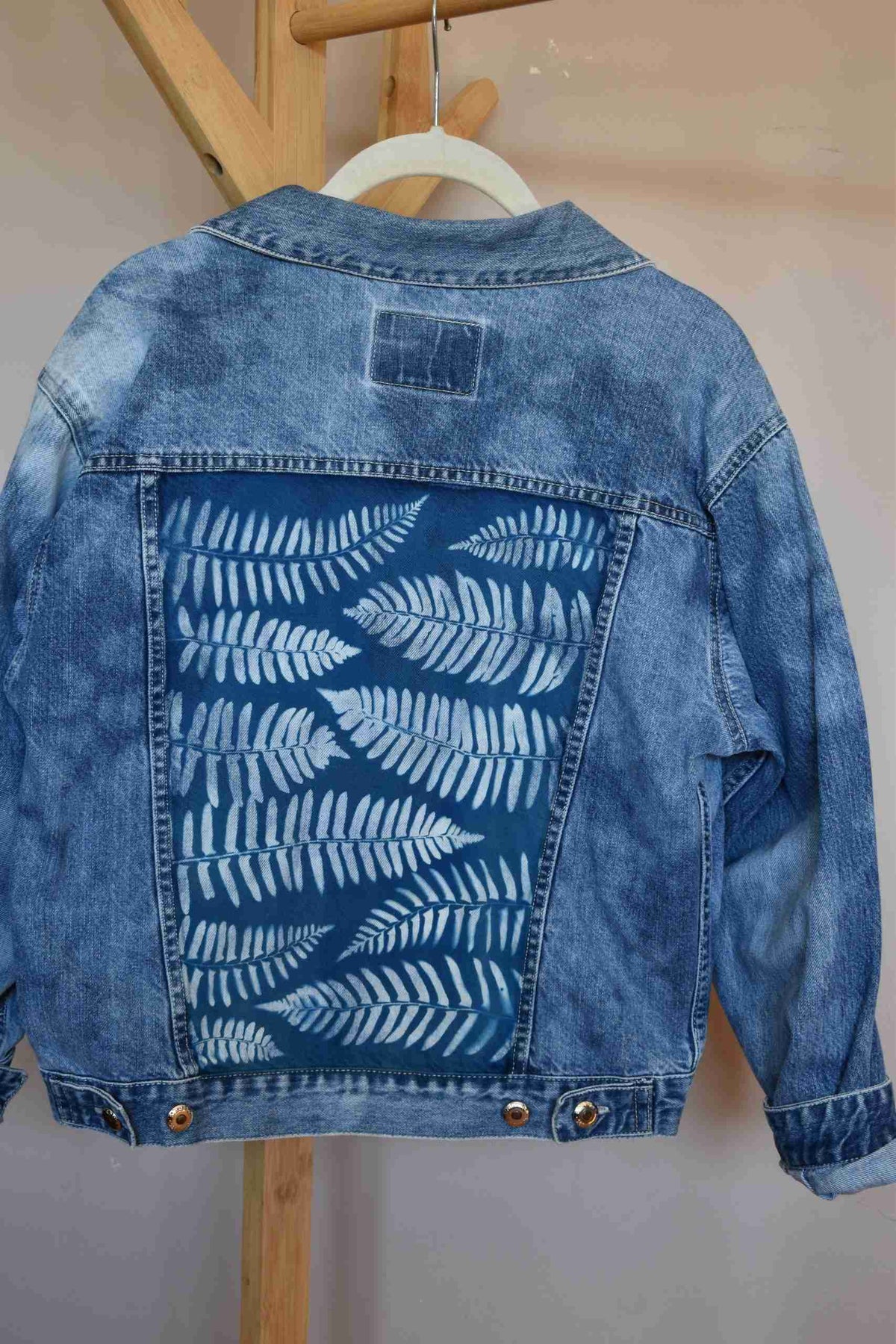 a blue jean jacket hanging on a wooden hanger.